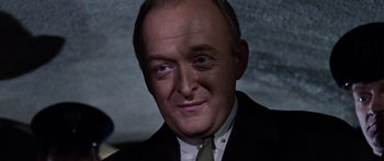 Movie still from “The Ipcress File” (1965), directed by Sidney J. Furie – A man with a green tie and a black suit; Close Up shot, High angle