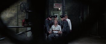 Movie still from “The Ipcress File” (1965), directed by Sidney J. Furie – A group of men standing next to each other in front of a building; Wide shot, Low angle