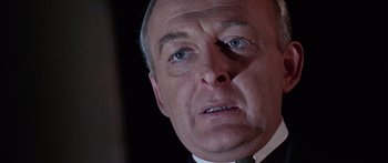 Movie still from “The Ipcress File” (1965), directed by Sidney J. Furie – An older man in a suit and tie looking at the camera; Close Up shot, Low angle