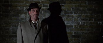 Movie still from “The Ipcress File” (1965), directed by Sidney J. Furie – A man wearing a hat and a coat standing in front of a brick wall; Close Up shot, Low angle