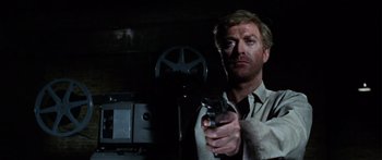 Movie still from “The Ipcress File” (1965), directed by Sidney J. Furie – A man holding a gun in a dark room; Close Up shot, Low angle