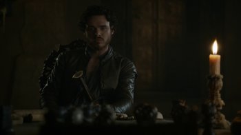 Movie still from “Game of Thrones” (2011), created by D.B. Weiss – A man sitting at a table with a spoon in his hand; Close Up shot, Over the shoulder angle