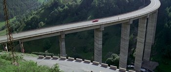 Movie still from “The Italian Job” (1969), directed by Peter Collinson – A red car is driving on a bridge over a river; Extreme Wide shot, High angle
