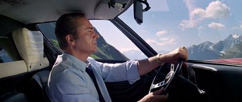 Movie still from “The Italian Job” (1969), directed by Peter Collinson – A man driving a car in the mountains; Medium shot, Low angle