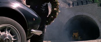 Movie still from “The Italian Job” (1969), directed by Peter Collinson – A man standing next to a motorcycle with a wreath of flowers on it; Wide shot, Low angle