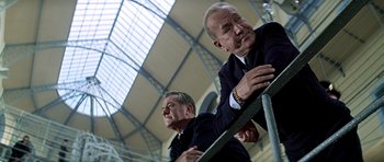 Movie still from “The Italian Job” (1969), directed by Peter Collinson – Two men in suits and ties sitting next to a railing; Medium shot, Low angle