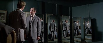 Movie still from “The Italian Job” (1969), directed by Peter Collinson – A man standing in front of a mirror in a suit and tie; Medium shot, Low angle