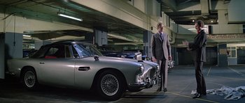 Movie still from “The Italian Job” (1969), directed by Peter Collinson – A man in a suit and tie standing next to some cars; Wide shot, Low angle