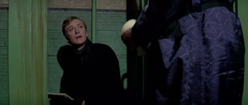 Movie still from “The Italian Job” (1969), directed by Peter Collinson – A man in a black jacket is looking at another man in a black jacket; Medium shot, Over the shoulder angle