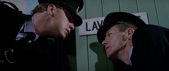 Movie still from “The Italian Job” (1969), directed by Peter Collinson – Two police officers face each other in front of a law sign; Close Up shot, Low angle