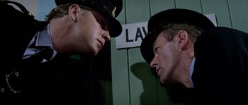 Movie still from “The Italian Job” (1969), directed by Peter Collinson – Two police officers are facing each other in front of a law sign; Close Up shot, Low angle