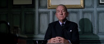 Movie still from “The Italian Job” (1969), directed by Peter Collinson – An older man sitting at a table in front of a painting; Close Up shot, Low angle