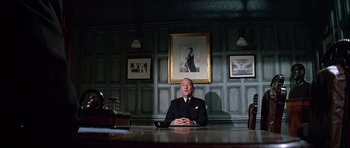 Movie still from “The Italian Job” (1969), directed by Peter Collinson – An older man sitting at a table in front of a painting; Medium shot, Low angle