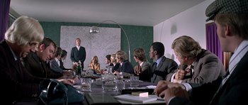 Movie still from “The Italian Job” (1969), directed by Peter Collinson – A group of people sitting around a table; Wide shot, Over the shoulder angle