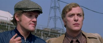 Movie still from “The Italian Job” (1969), directed by Peter Collinson – Two men standing next to each other in front of power lines; Close Up shot, Low angle