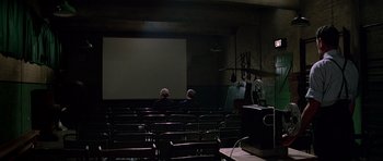Movie still from “The Italian Job” (1969), directed by Peter Collinson – Two men are sitting in front of a projection screen; Wide shot, High angle