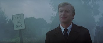 Movie still from “The Italian Job” (1969), directed by Peter Collinson – A man wearing a suit and tie standing in front of trees; Close Up shot, Low angle