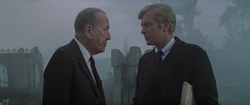Movie still from “The Italian Job” (1969), directed by Peter Collinson – Two men in suits talking to each other outside; Medium shot, Low angle