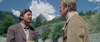 Movie still from “The Italian Job” (1969), directed by Peter Collinson – Two men are standing in front of a mountain; Medium shot, Over the shoulder angle