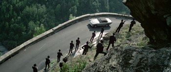 Movie still from “The Italian Job” (1969), directed by Peter Collinson – A group of people standing on a hill next to a car; Extreme Wide shot, High angle