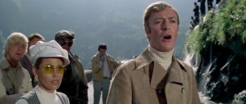 Movie still from “The Italian Job” (1969), directed by Peter Collinson – A man in a tan jacket is standing next to two other men; Close Up shot, Low angle
