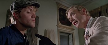 Movie still from “The Italian Job” (1969), directed by Peter Collinson – Two people are talking in a room with a painting; Close Up shot, Over the shoulder angle