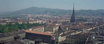 Movie still from “The Italian Job” (1969), directed by Peter Collinson – An aerial view of a large city with buildings and mountains in the background; Extreme Wide shot, High angle