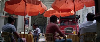 Movie still from “The Italian Job” (1969), directed by Peter Collinson – Two people sitting at a table under red umbrellas on the street; Wide shot, High angle