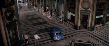 Movie still from “The Italian Job” (1969), directed by Peter Collinson – A blue car driving down a street next to people; Extreme Wide shot, High angle