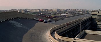 Movie still from “The Italian Job” (1969), directed by Peter Collinson – Cars are parked along a road with a person on a motorcycle on the side of the road; Extreme Wide shot, High angle