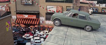 Movie still from “The Italian Job” (1969), directed by Peter Collinson – A car is parked on the side of the street; Extreme Wide shot, High angle