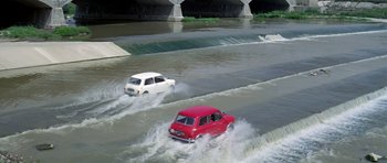 Movie still from “The Italian Job” (1969), directed by Peter Collinson – A red car and a white car driving through a flooded area; Extreme Wide shot, High angle