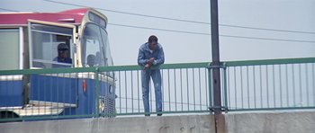 Movie still from “The Italian Job” (1969), directed by Peter Collinson – A man leaning on a railing near a bus; Wide shot, Low angle