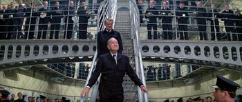 Movie still from “The Italian Job” (1969), directed by Peter Collinson – A man in a suit and tie standing next to another man in a suit and tie; Wide shot, Low angle