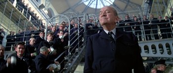 Movie still from “The Italian Job” (1969), directed by Peter Collinson – A man in a suit and tie in front of a group of people; Medium shot, Low angle