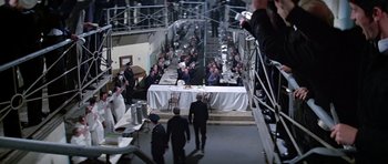 Movie still from “The Italian Job” (1969), directed by Peter Collinson – A group of people standing around a table with food on it; Extreme Wide shot, High angle