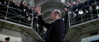 Movie still from “The Italian Job” (1969), directed by Peter Collinson – An older man in a suit and tie clapping in front of a group of people; Medium shot, Low angle