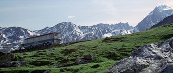 Movie still from “The Italian Job” (1969), directed by Peter Collinson – A view of a snowy mountain from a grassy hill; Extreme Wide shot, Low angle