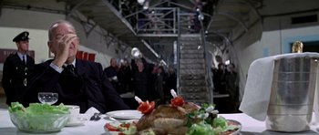 Movie still from “The Italian Job” (1969), directed by Peter Collinson – A table topped with a plate of food next to a bunch of people; Medium shot, High angle