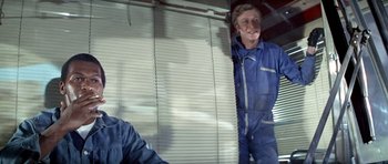 Movie still from “The Italian Job” (1969), directed by Peter Collinson – A man in blue coveralls standing next to a window; Medium shot, Low angle