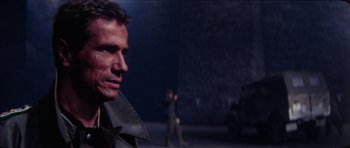 Movie still from “The Keep” (1983), directed by Michael Mann – A man standing in front of another man in a dark room; Close Up shot, Over the shoulder angle