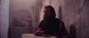 Movie still from “The Keep” (1983), directed by Michael Mann – A man sitting at a table with a cigarette in his mouth; Medium shot, Low angle