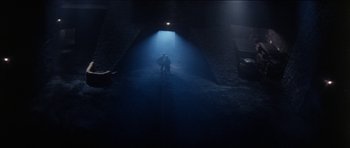 Movie still from “The Keep” (1983), directed by Michael Mann – A person standing in a dark room with a light shining on them; Extreme Wide shot, Low angle