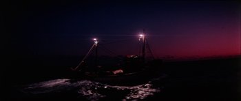 Movie still from “The Keep” (1983), directed by Michael Mann – A boat in the water at night with lights on; Extreme Wide shot, Low angle