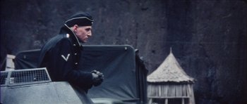 Movie still from “The Keep” (1983), directed by Michael Mann – A man in a military uniform standing next to a tent; Medium shot, Over the shoulder angle