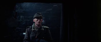 Movie still from “The Keep” (1983), directed by Michael Mann – A man wearing a uniform and a hat is in a dark room; Medium shot, Low angle