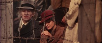 Movie still from “The Keep” (1983), directed by Michael Mann – A woman wearing a red hat sitting next to a fence; Close Up shot, Over the shoulder angle