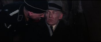 Movie still from “The Keep” (1983), directed by Michael Mann – An older man wearing a suit and a hat; Close Up shot, Over the shoulder angle