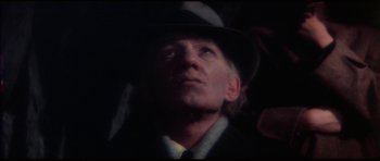 Movie still from “The Keep” (1983), directed by Michael Mann – A person wearing a hat and a suit; Close Up shot, Low angle