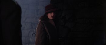 Movie still from “The Keep” (1983), directed by Michael Mann – A woman wearing a brown coat and a red hat; Close Up shot, Over the shoulder angle